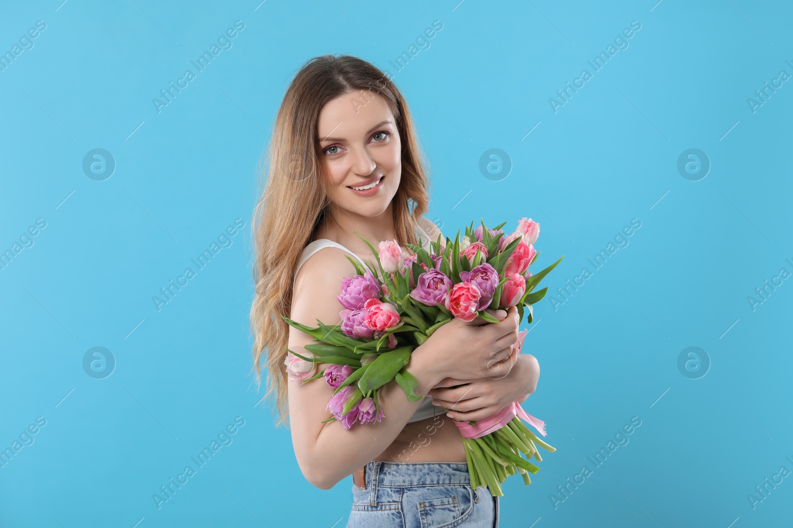 Photo of Happy young woman with bouquet of beautiful tulips on light blue background