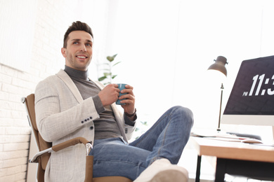 Photo of Young man with cup of drink relaxing at table in office during break