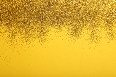 Photo of Shiny golden glitter on yellow background, top view. Space for text