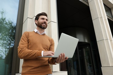 Photo of Handsome man with laptop near building on city street