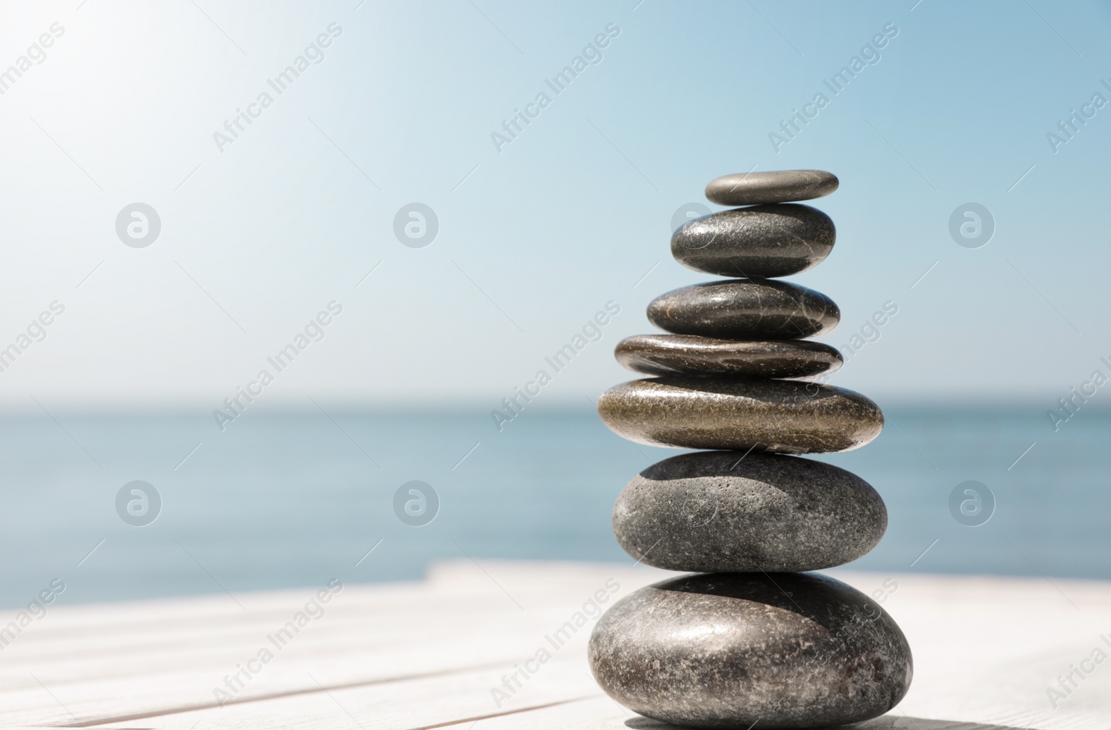 Photo of Stack of stones on wooden pier near sea, space for text. Zen concept