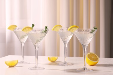 Photo of Martini glasses with fresh cocktail, rosemary and lemon on white table indoors