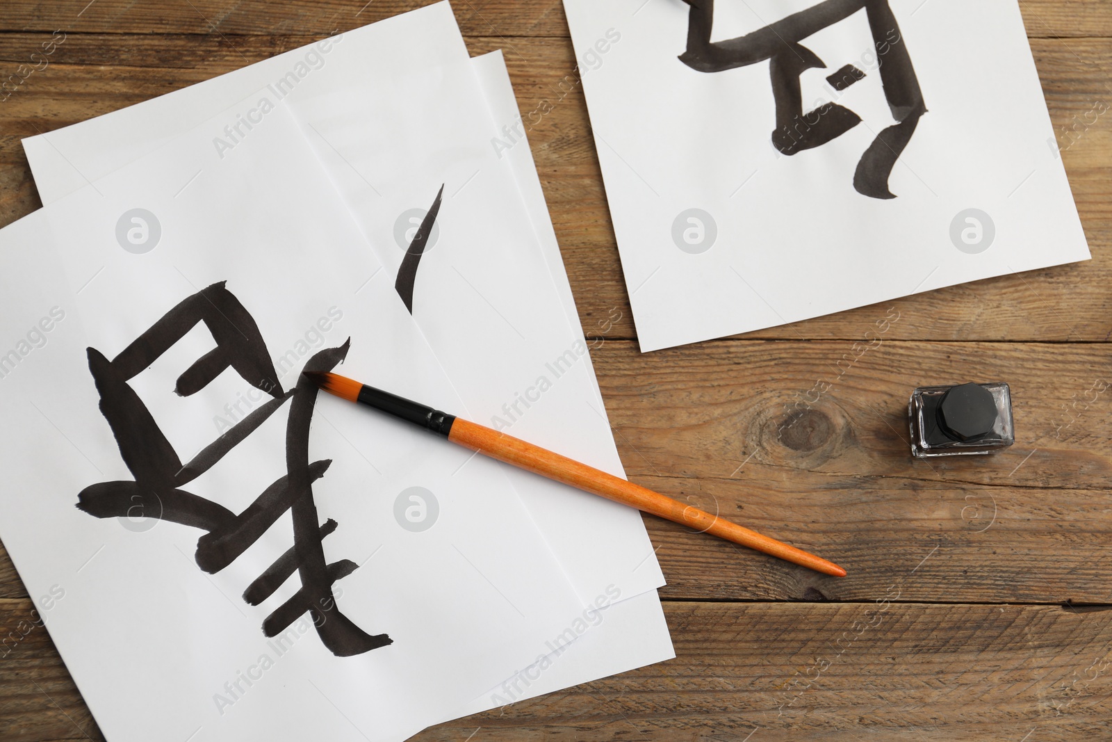 Photo of Calligraphy. Papers with written hieroglyphs, inkwell and brush on wooden table, flat lay