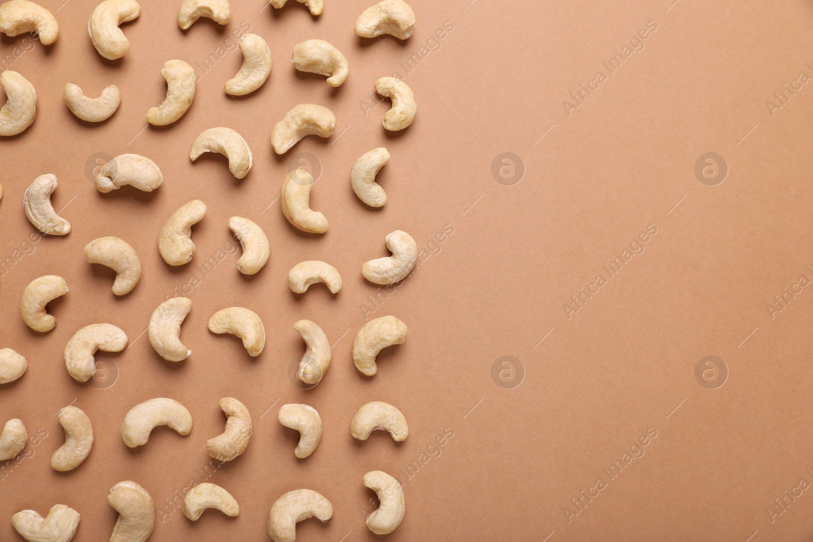 Photo of Many tasty cashew nuts on pale brown background, top view. Space for text