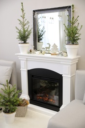 Little fir trees and Christmas decorations in room with fireplace. Stylish interior design