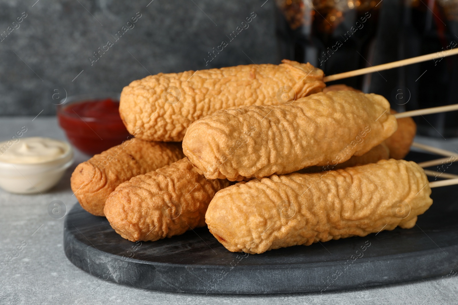 Photo of Delicious deep fried corn dogs with board and sauces on light grey table, closeup