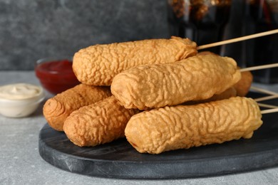 Delicious deep fried corn dogs with board and sauces on light grey table, closeup