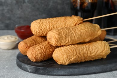 Photo of Delicious deep fried corn dogs with board and sauces on light grey table, closeup