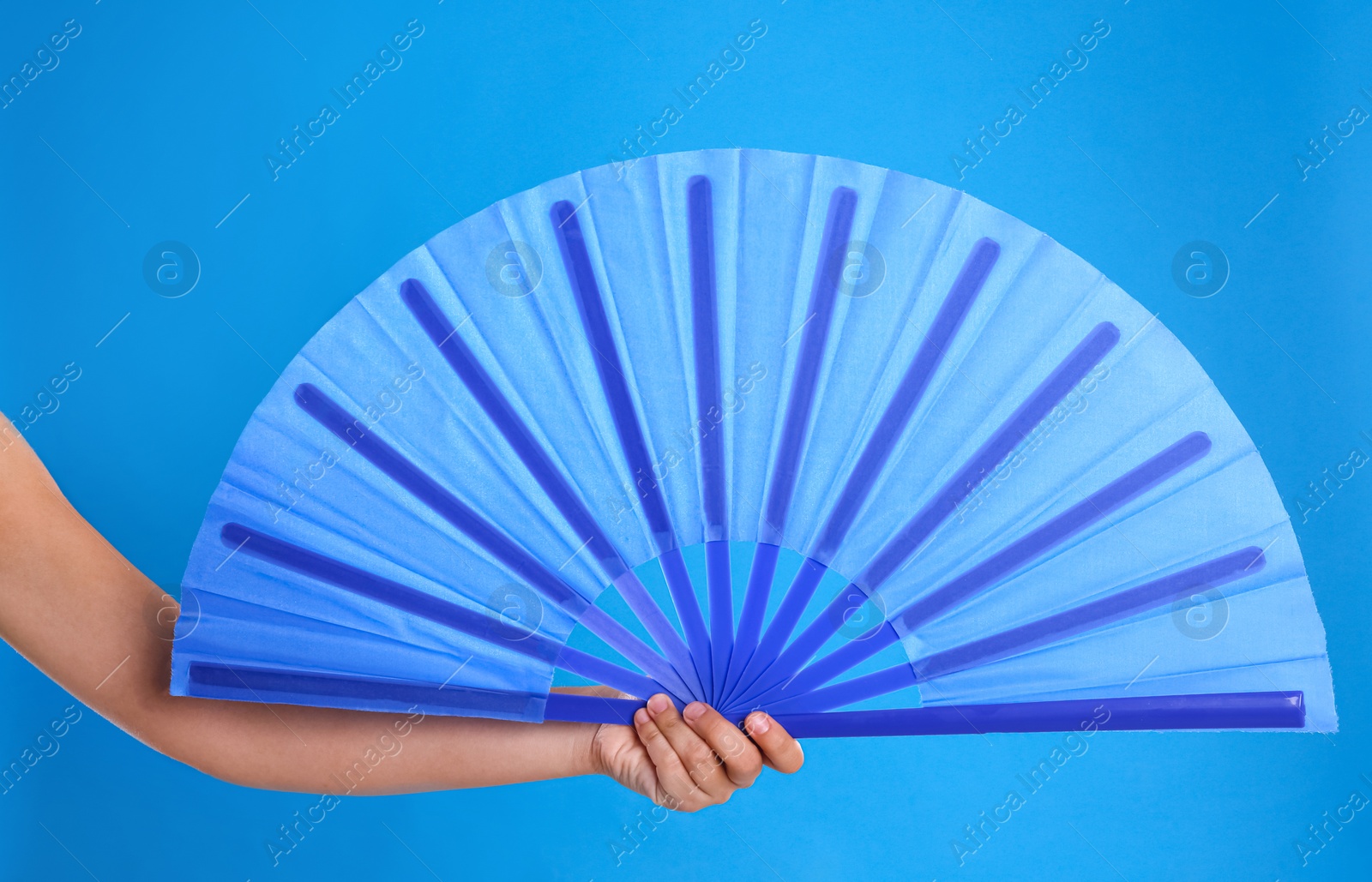 Photo of Woman holding hand fan on light blue background, closeup