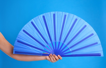 Photo of Woman holding hand fan on light blue background, closeup