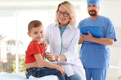 Children's doctor examining little boy with stethoscope in hospital