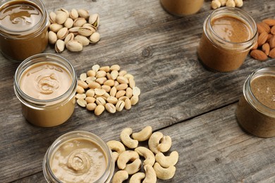 Photo of Tasty nut butters in jars and raw nuts on wooden table