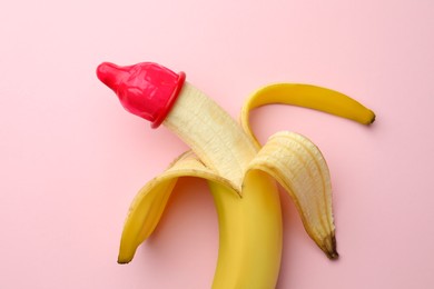 Photo of Banana with condom on pink background, top view. Safe sex concept