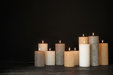 Alight wax candles on table against dark background. Space for text