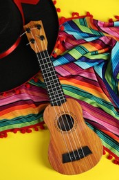 Black Flamenco hat, poncho and ukulele on yellow table, flat lay