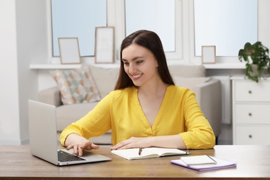 Happy young woman with notebook working on laptop at wooden table indoors