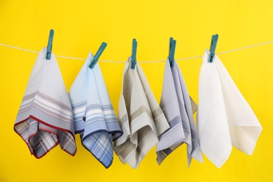 Photo of Many different handkerchiefs hanging on rope against yellow background