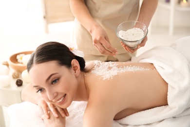 Beautiful young woman having massage with body scrub in spa salon