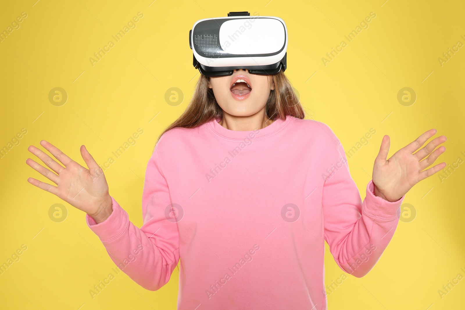 Photo of Emotional young woman playing video games with virtual reality headset on color background