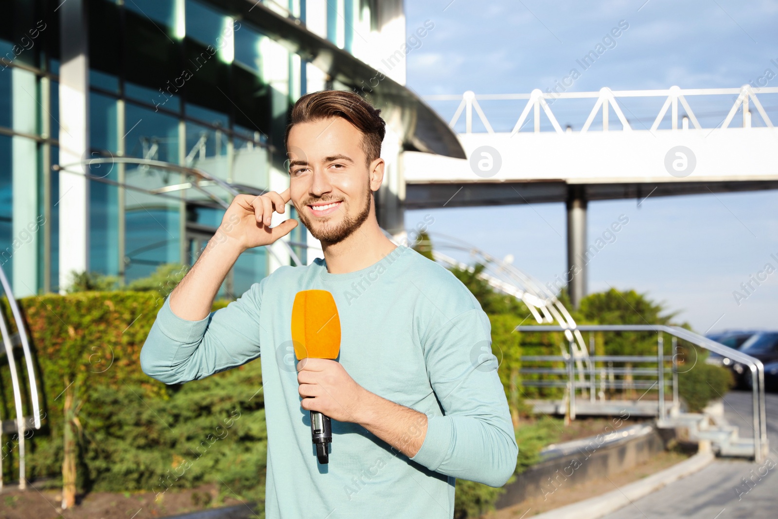 Photo of Young male journalist with microphone working on city street