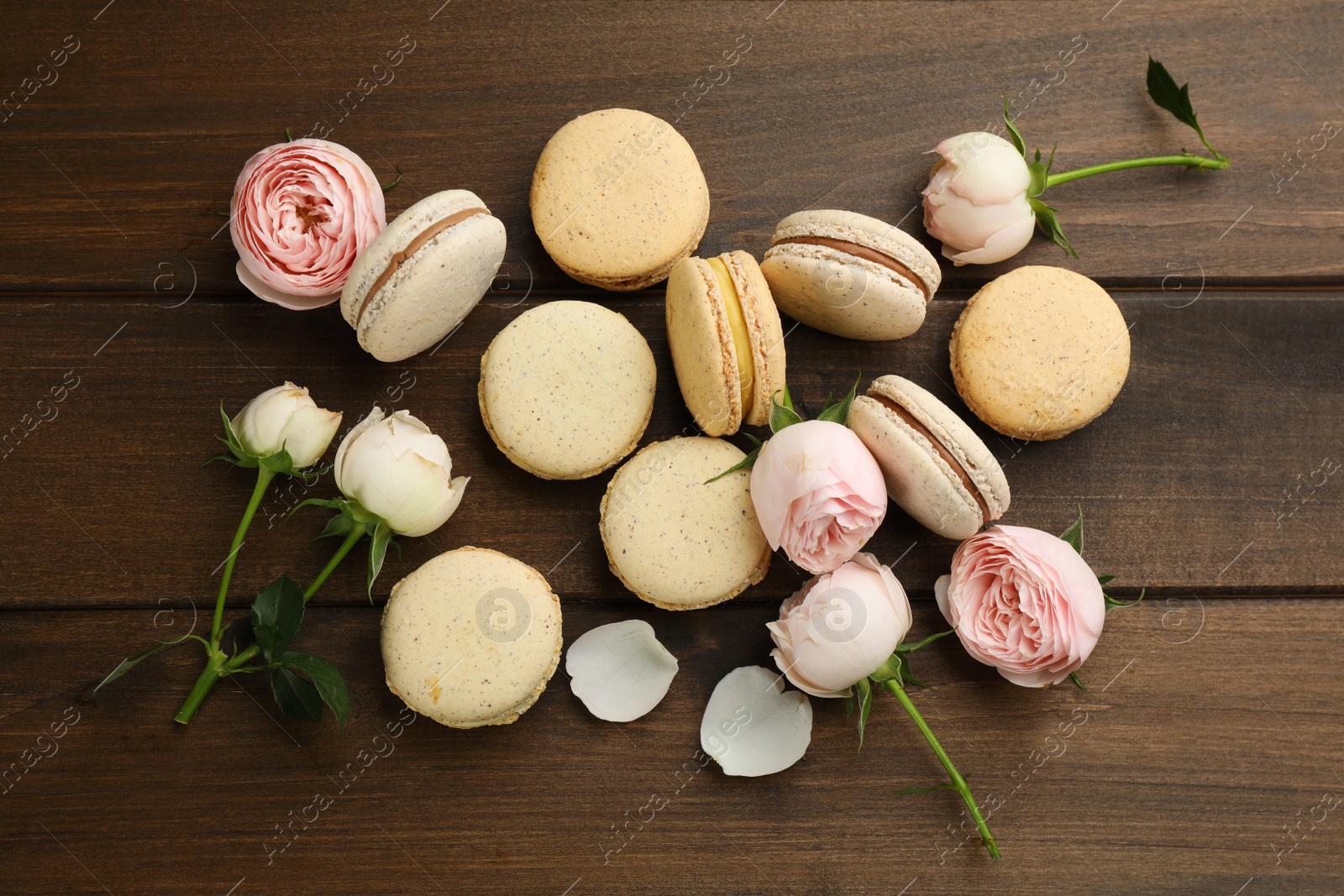 Photo of Delicious macarons and flowers on wooden table, flat lay