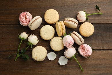 Photo of Delicious macarons and flowers on wooden table, flat lay