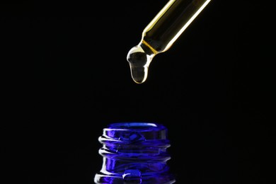 Photo of Dripping tincture from pipette into bottle on black background, closeup