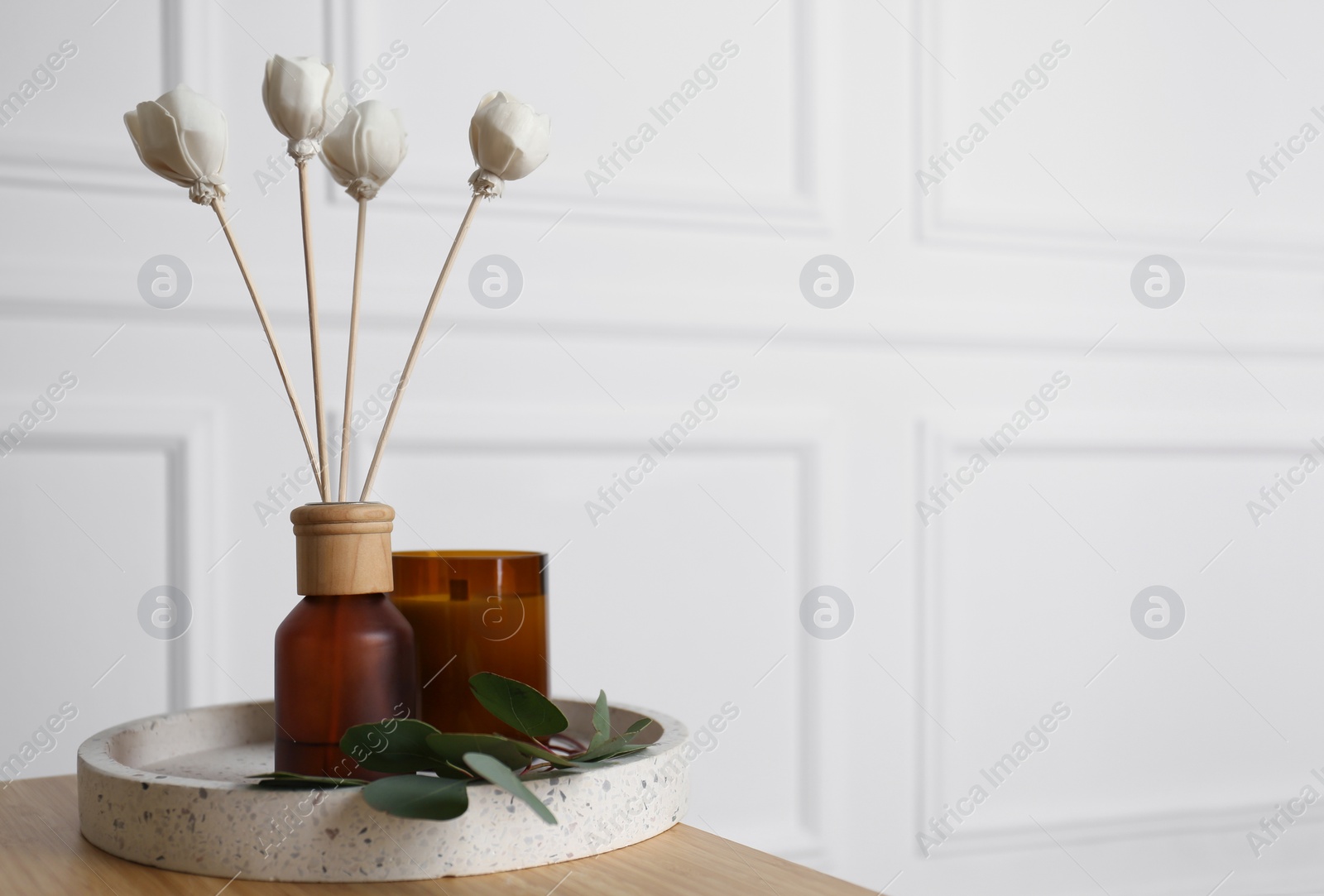 Photo of Reed air freshener with candle and eucalyptus branch on tray indoors. Space for text