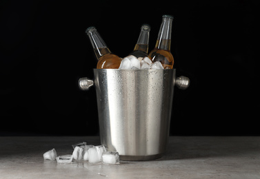 Photo of Metal bucket with bottles of beer and ice cubes on grey table