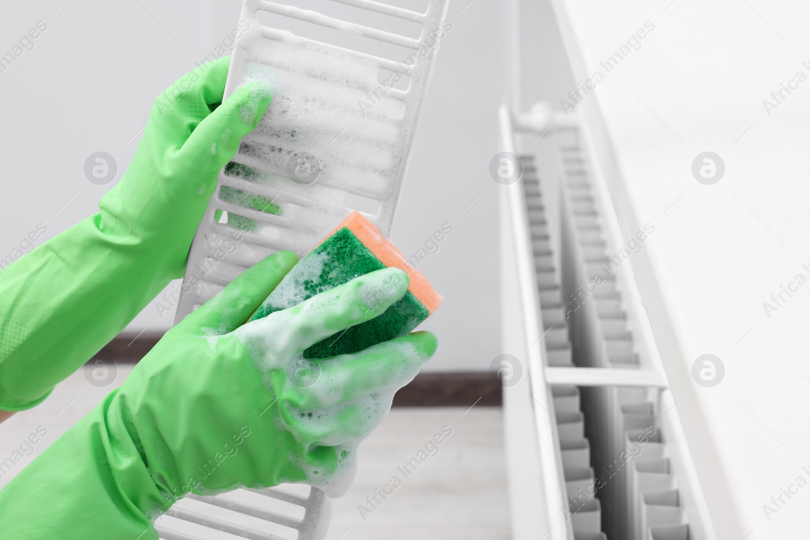 Photo of Woman washing radiator grill with sponge and detergent indoors, closeup