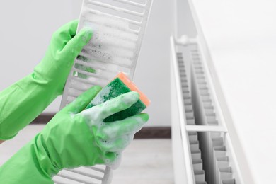 Woman washing radiator grill with sponge and detergent indoors, closeup