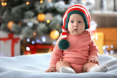 Little baby wearing elf hat on blanket indoors. First Christmas