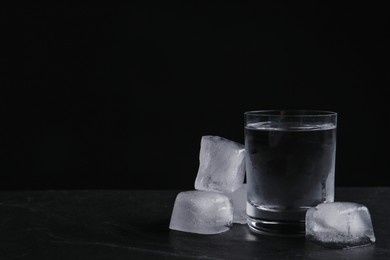 Photo of Vodka in shot glass with ice on table against black background. Space for text