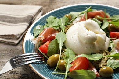 Photo of Delicious burrata salad served on wooden table, closeup