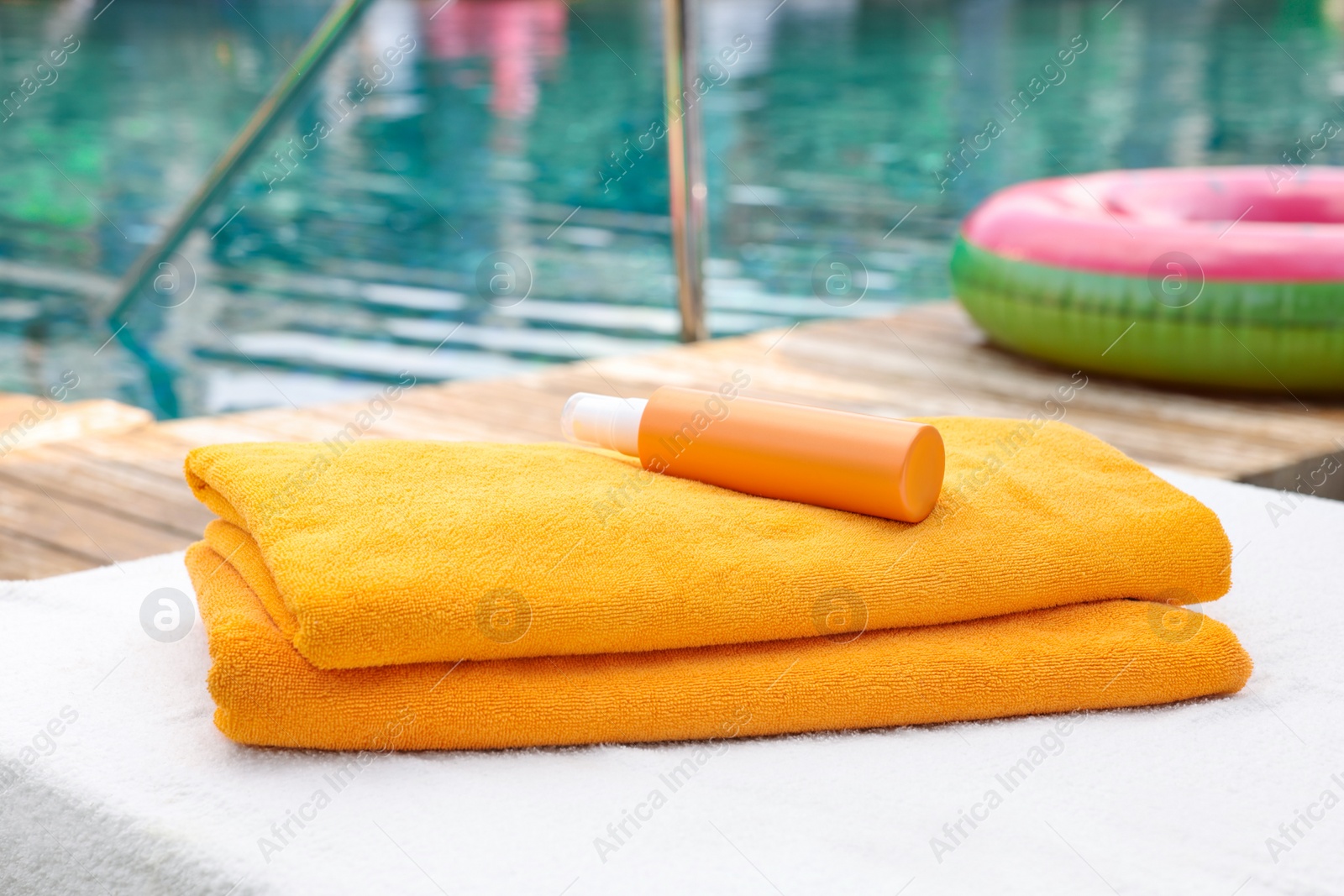 Photo of Beach towels and sunscreen on sun lounger near outdoor swimming pool, selective focus. Luxury resort