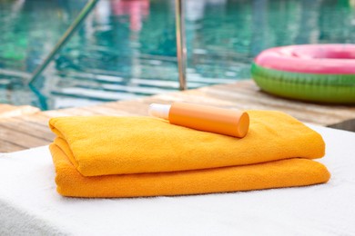 Beach towels and sunscreen on sun lounger near outdoor swimming pool, selective focus. Luxury resort