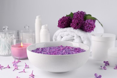 Photo of Bowl of water with lilac flowers, spa products and burning candle on white table
