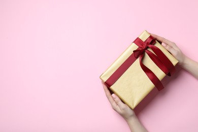 Photo of Christmas present. Woman holding gift box on pink background, top view. Space for text