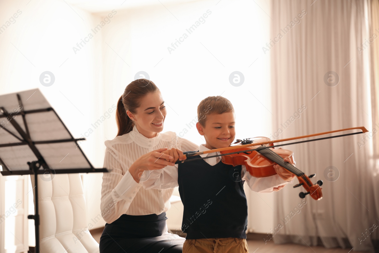 Photo of Young woman teaching little boy to play violin indoors