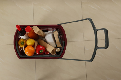 Shopping basket full of different products on beige tile floor, top view