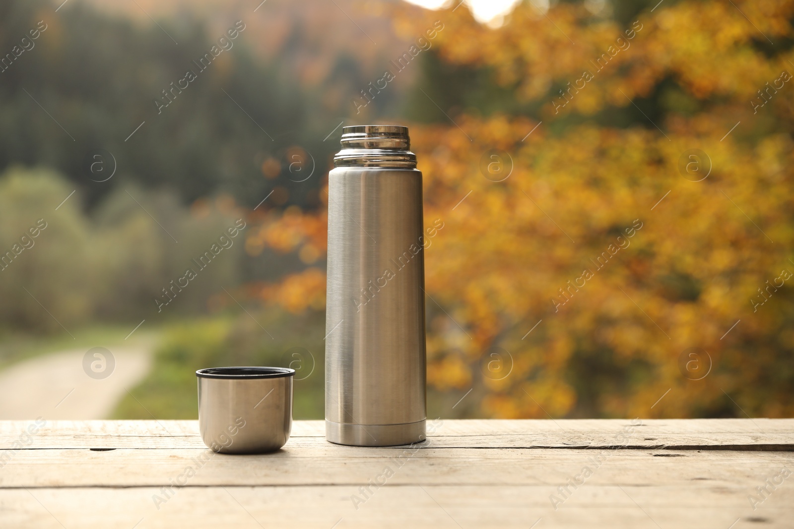 Photo of Metallic thermos and cup lid on wooden table outdoors, space for text