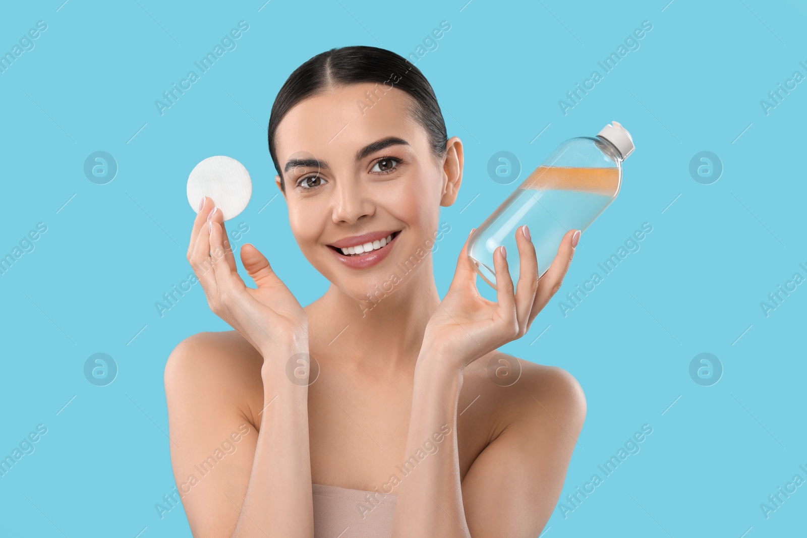 Photo of Beautiful woman holding makeup remover and cotton pad on light blue background