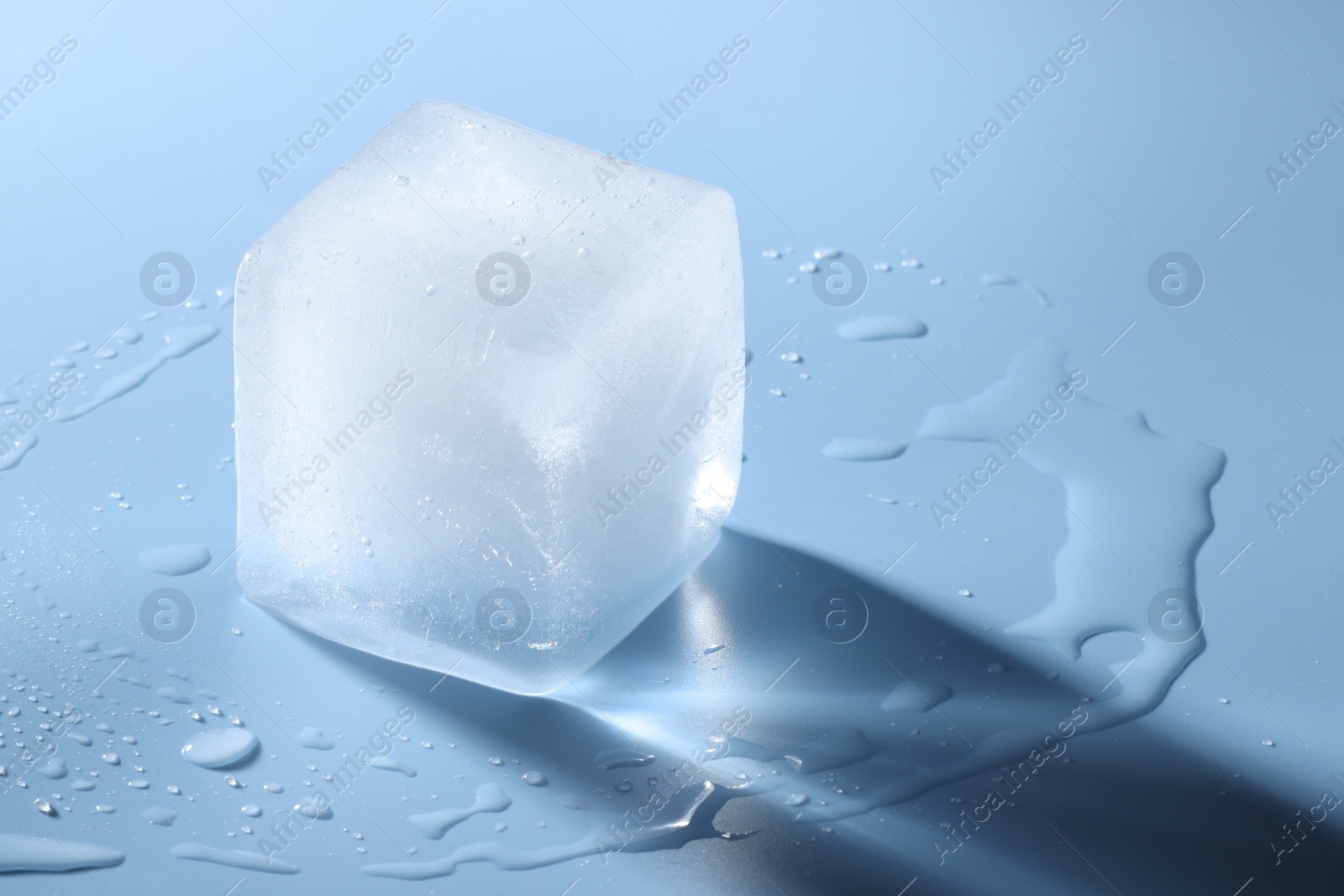 Photo of Crystal clear ice cube on light blue background, space for text