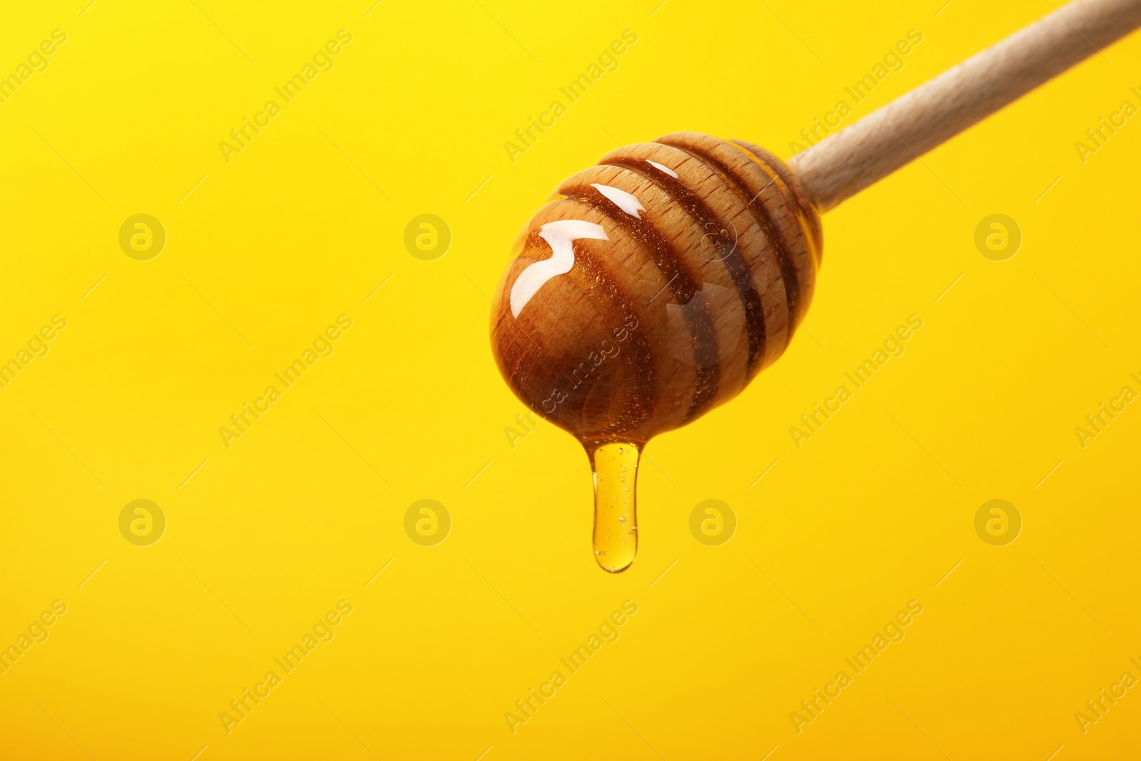 Photo of Pouring honey from dipper against yellow background, closeup. Space for text