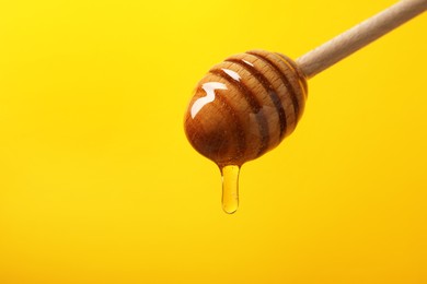 Pouring honey from dipper against yellow background, closeup. Space for text