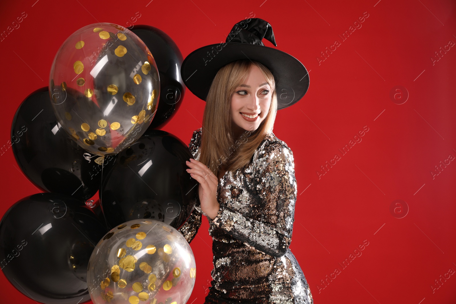 Photo of Beautiful woman in witch costume with balloons on red background. Halloween party