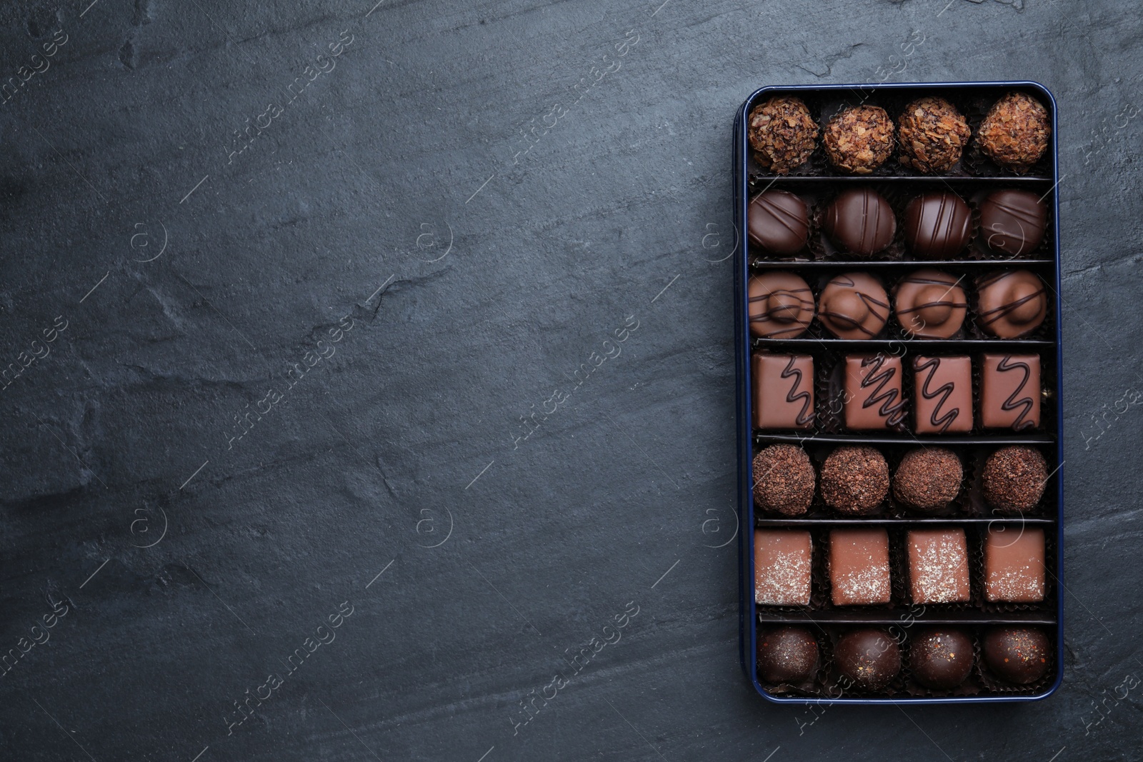 Photo of Box with delicious chocolate candies on black table, top view. Space for text