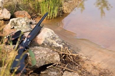 Photo of Hunting rifle and cartridges on rocks near lake outdoors. Space for text