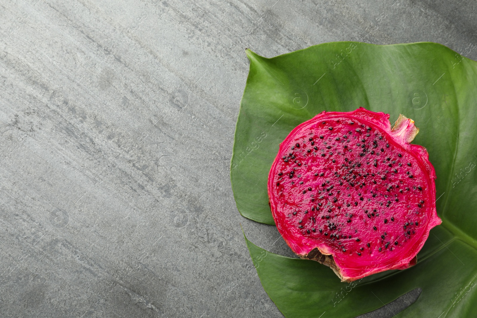 Photo of Delicious cut red pitahaya fruit and green leaf on grey table, flat lay. Space for text