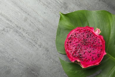 Photo of Delicious cut red pitahaya fruit and green leaf on grey table, flat lay. Space for text